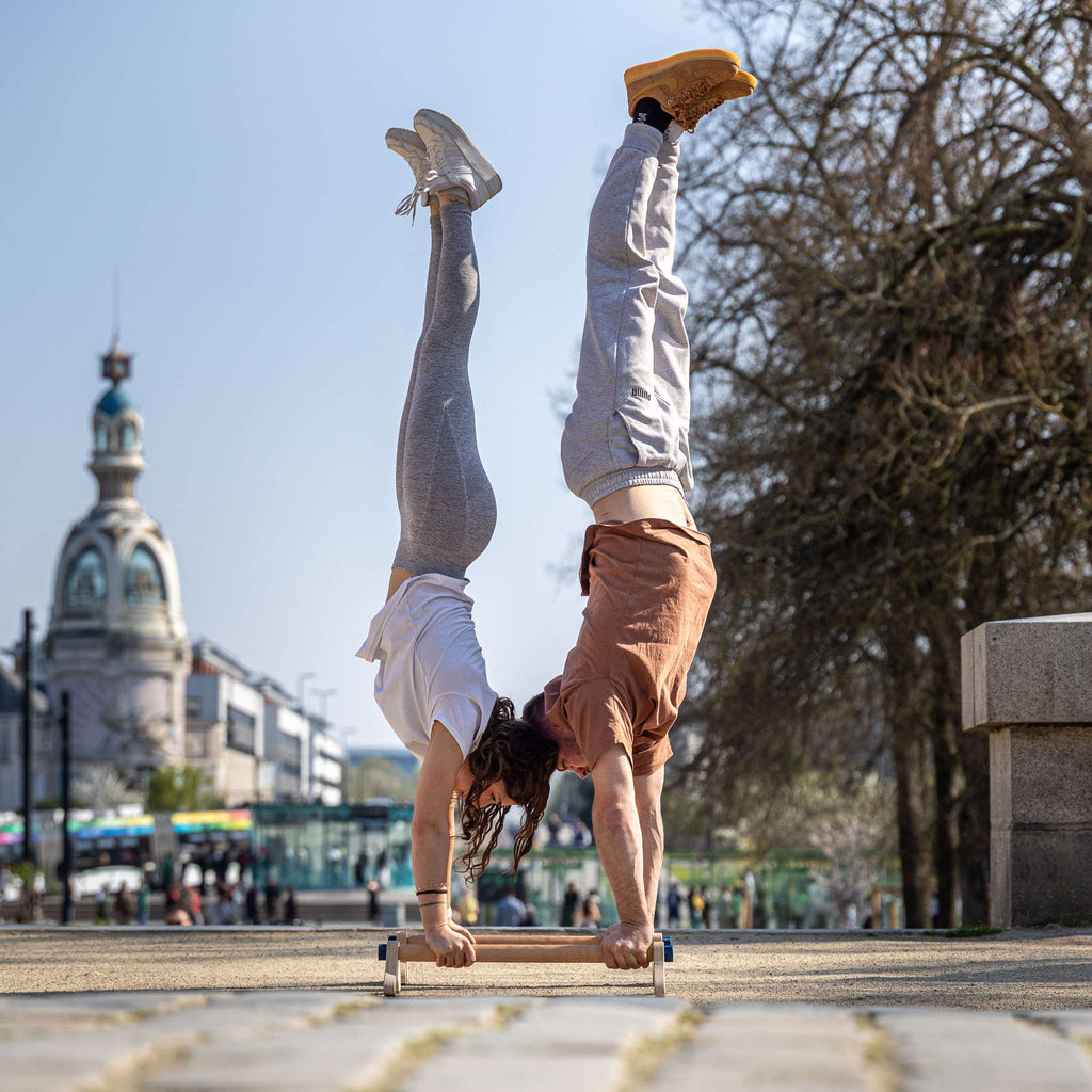 photo de deux personnes réalisant un équilibre sur les mains sur les mêmes parallettes Peisma de 60 cm avec Nantes en arrière pla