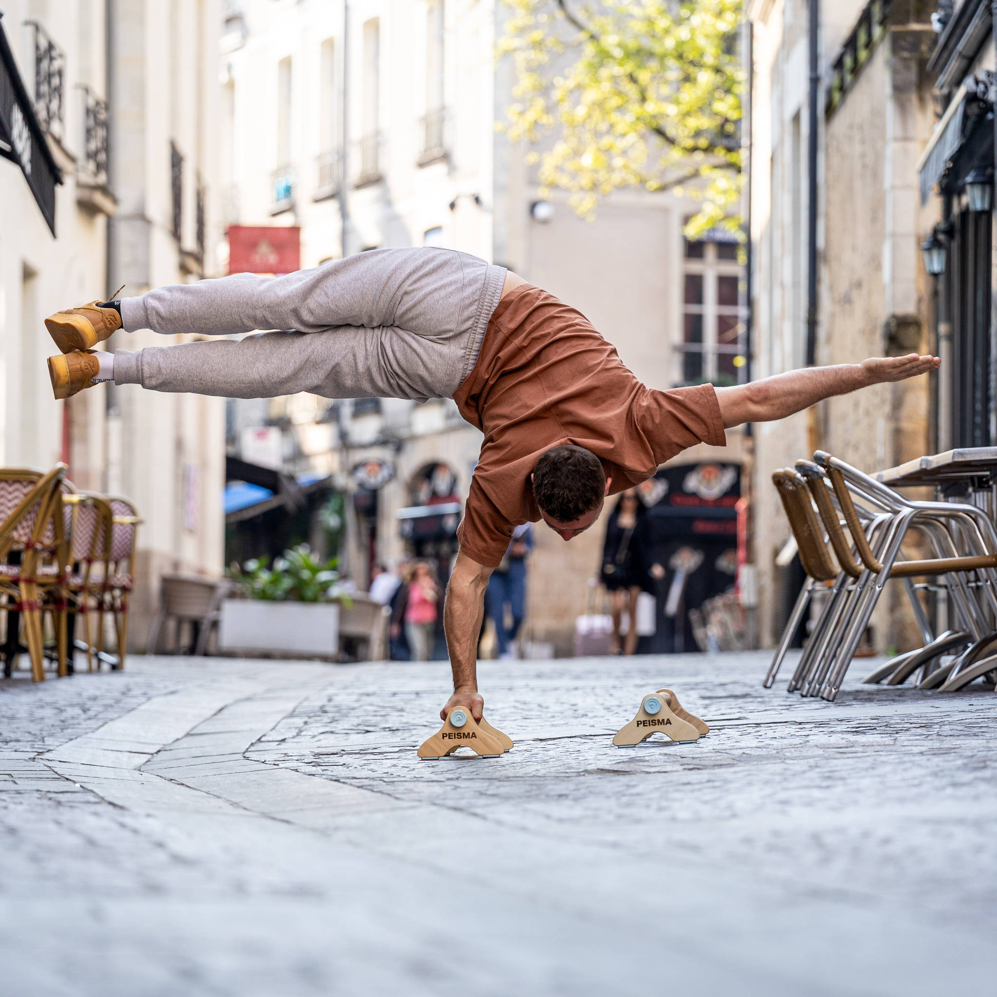une personne dans une ruelle faisant un équilibre sur une main sur des parallettes Peisma