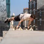Une personne faisant la figure de la full planche sur des parallettes Peismadans la ville