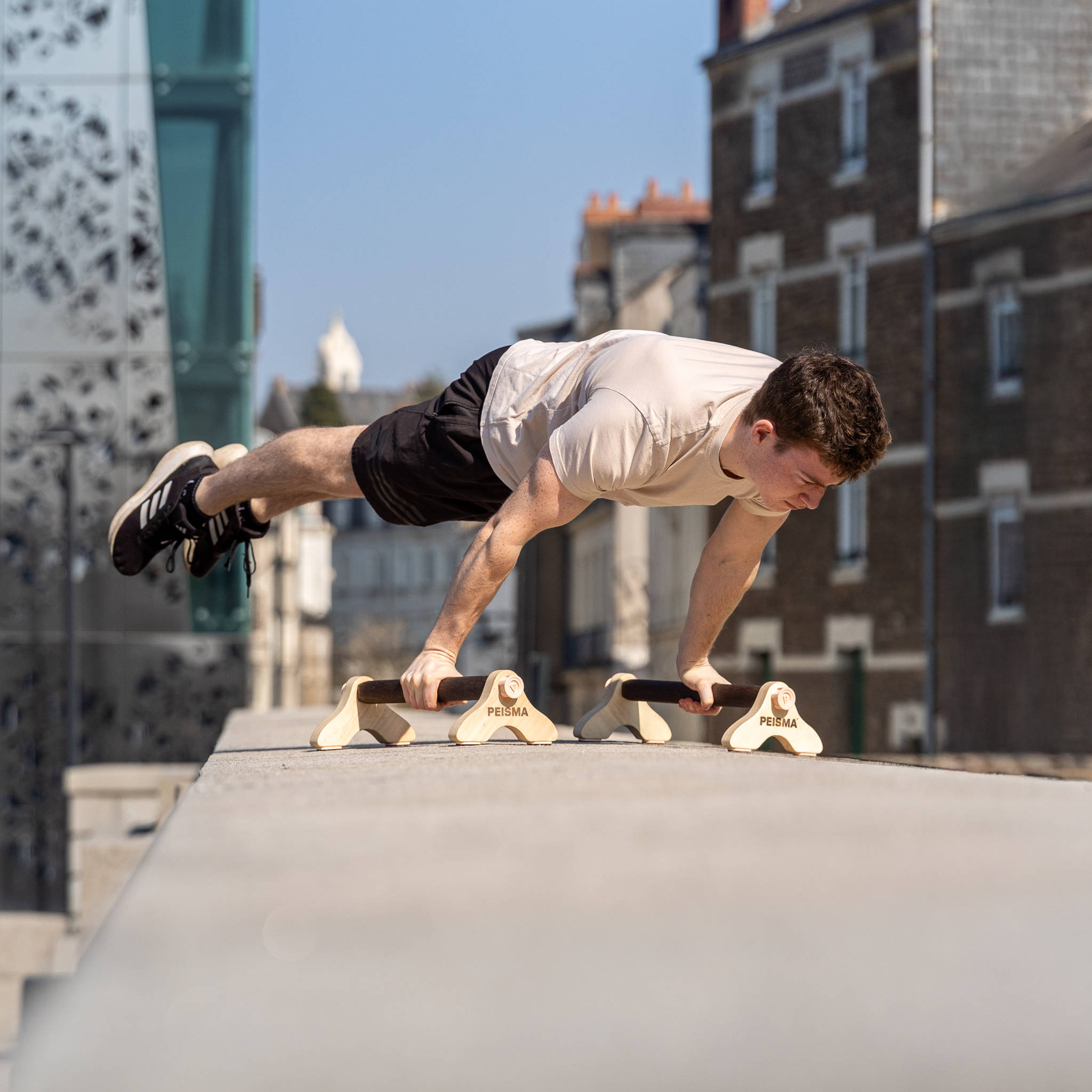 Une personne faisant la figure de la full planche sur des parallettes Peismadans la ville
