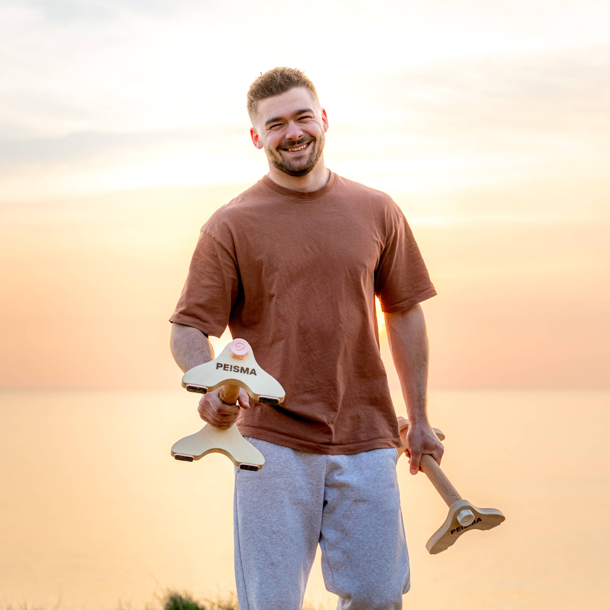 une personne souriante montrant des parallettes Peisma avec la mer et le couché de soleil en arrière plan