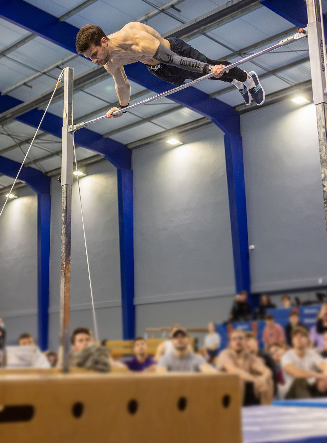 Photo de Mattéo Riffault d'un athlète testeur en pleine performance sur une barre fixe dans une salle de gym avec les regards tournés vers lui.