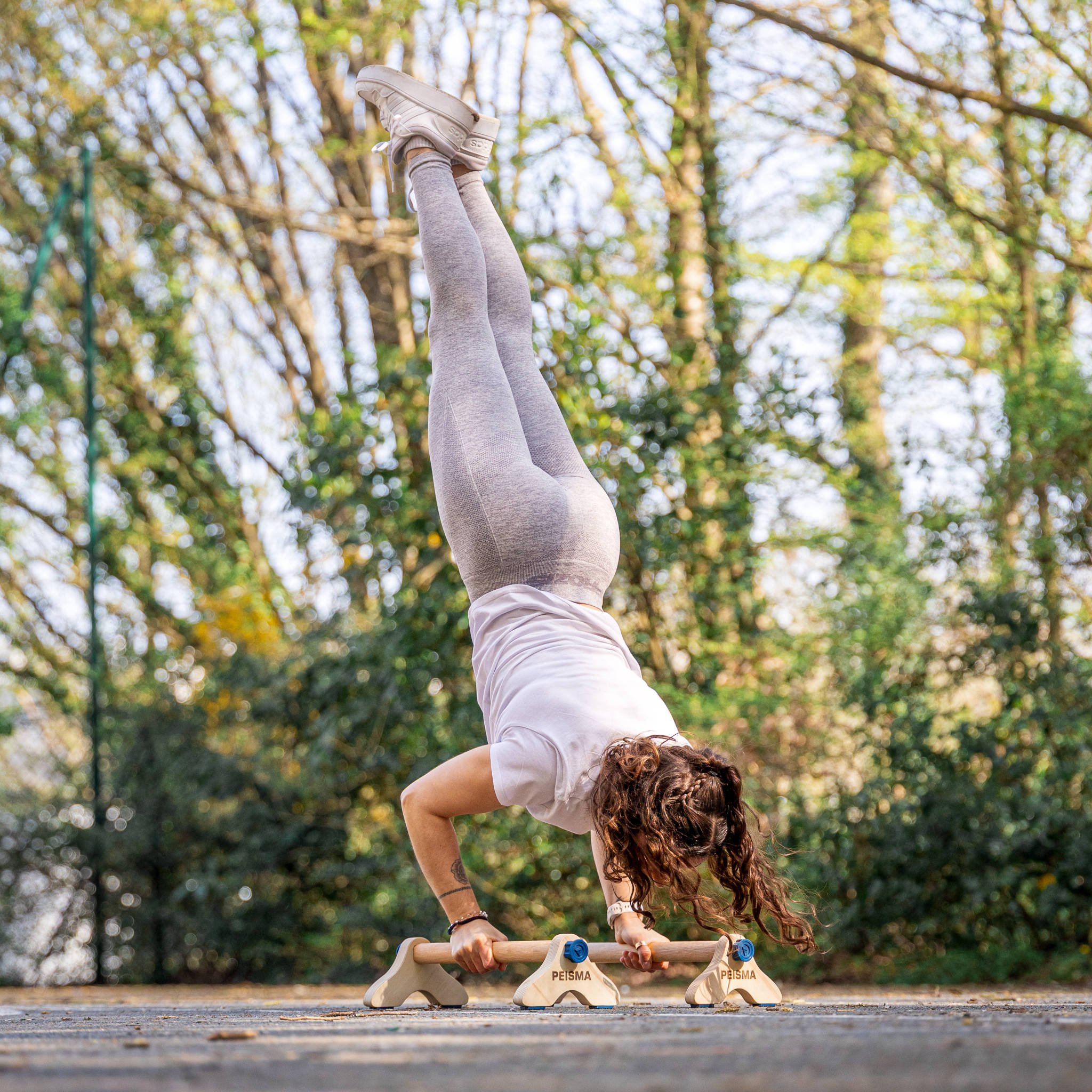 photo d'une femme en train de faire une pompe en équilibre sur des parallettes Peisma sur un terrain de basket en béton